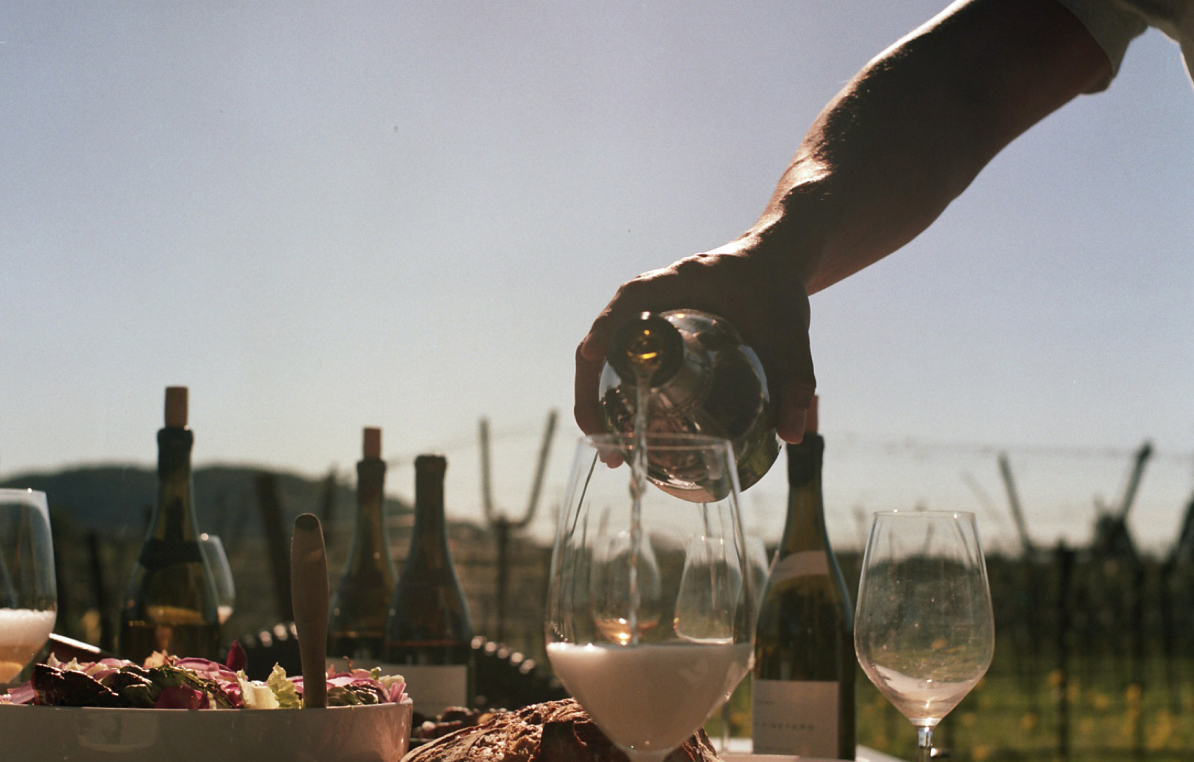 Man pouring wine at an outdoor meal by the vineyard